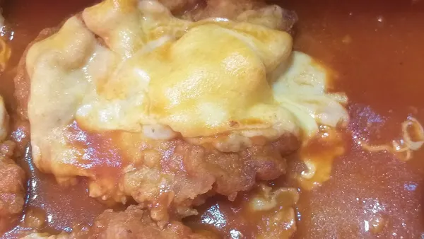 Bife à parmegiana com casca dourada coberta de molho de tomate e queijo gratinado borbulhando, cortado mostrando a carne macia