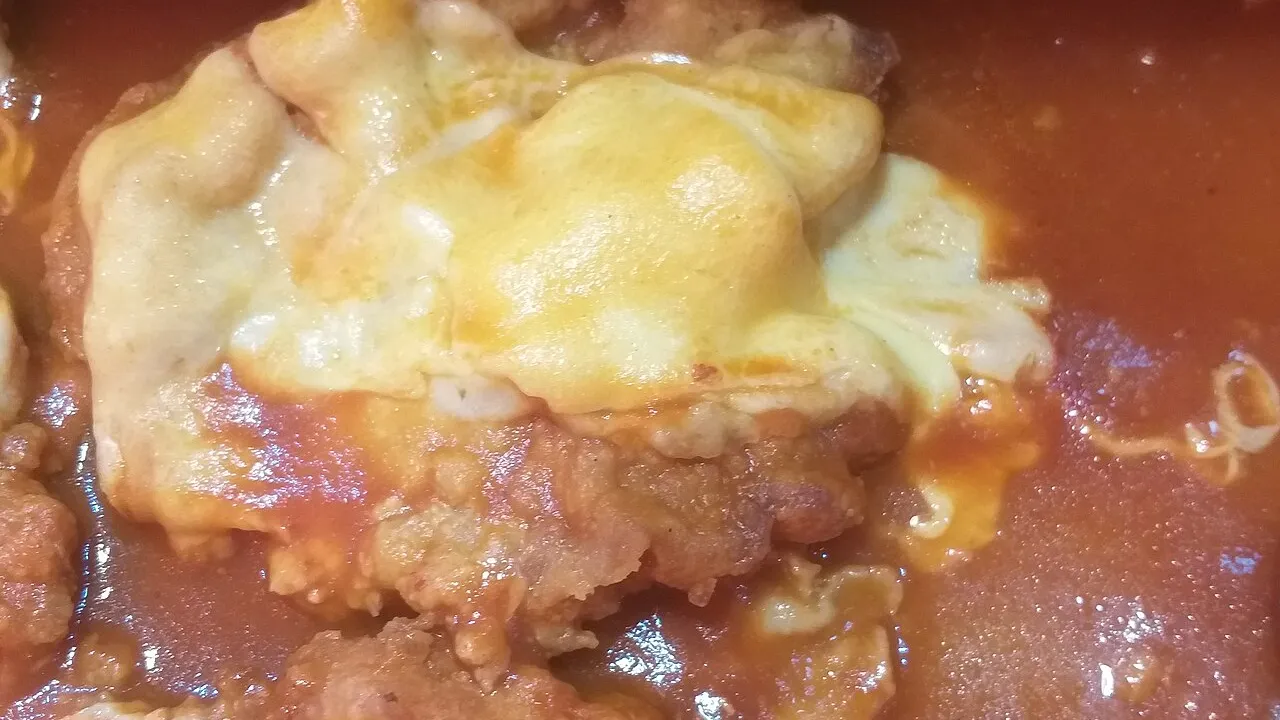 Bife à parmegiana com casca dourada coberta de molho de tomate e queijo gratinado borbulhando, cortado mostrando a carne macia