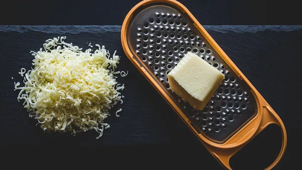 Pote de vidro com frango desfiado úmido e dourado, ao lado de garfo usado para desfiar