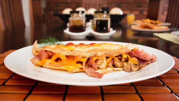 Omelete amarela dobrada ao meio num prato, macia e brilhante, sem bordas queimadas