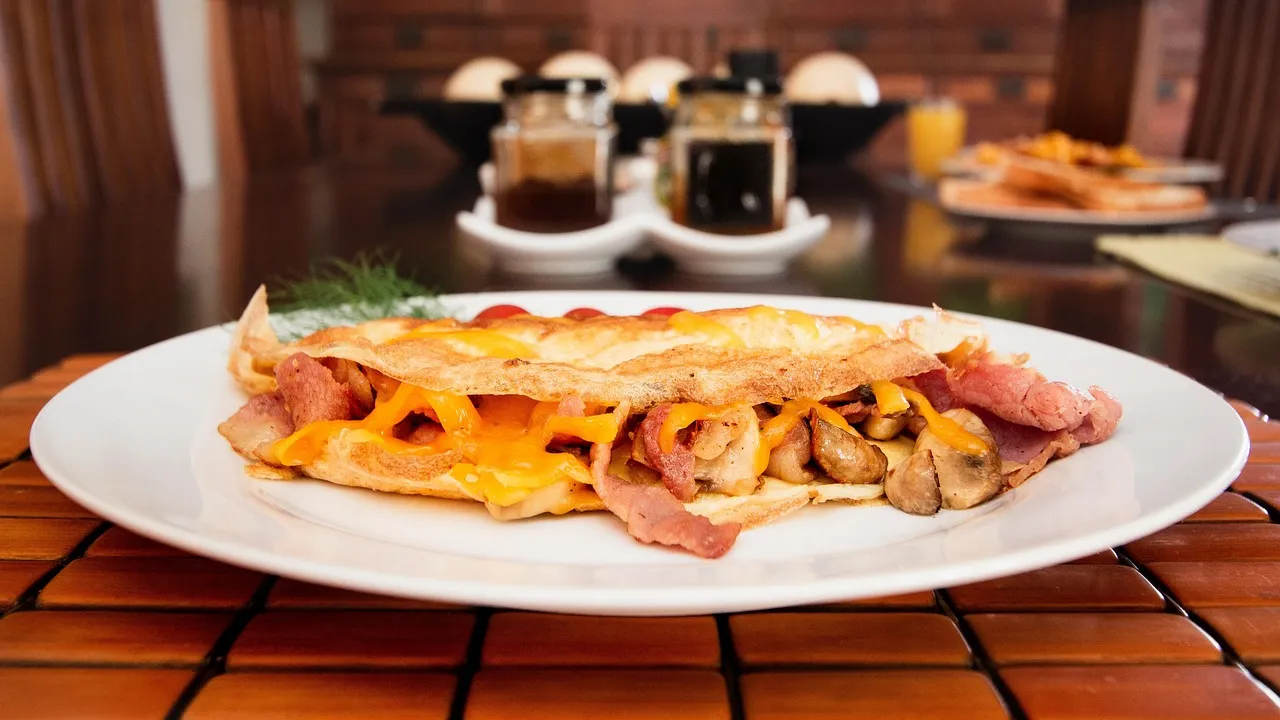 Omelete amarela dobrada ao meio num prato, macia e brilhante, sem bordas queimadas
