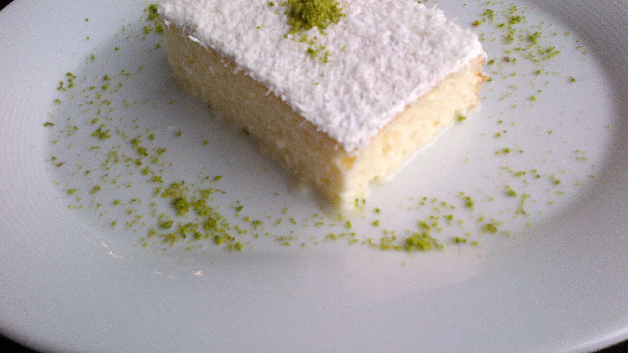 Fatia de bolo de coco cremoso com cobertura de coco ralado sobre prato branco