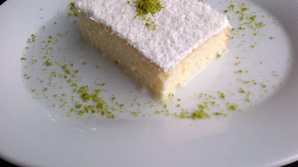Fatia de bolo de coco cremoso com cobertura de coco ralado sobre prato branco