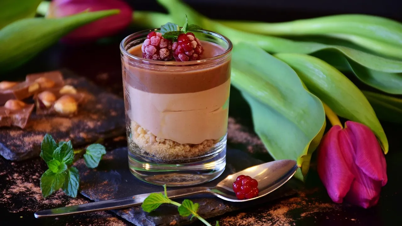 Taça de vidro com mousse de maracujá amarelo-clara e cremosa, coberta com calda de maracujá com sementes por cima