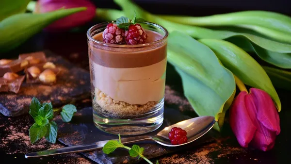 Taça de vidro com mousse de maracujá amarelo-clara e cremosa, coberta com calda de maracujá com sementes por cima