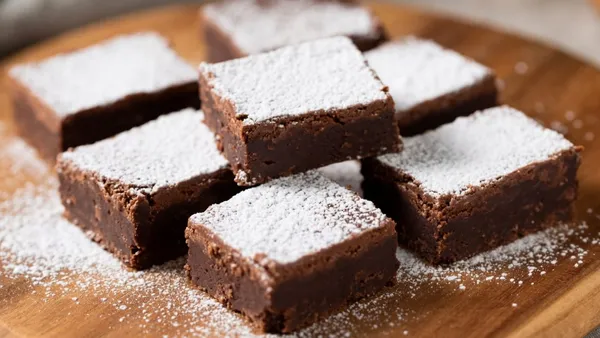 Quadrados de doce de chocolate com biscoito polvilhados com açúcar de confeiteiro sobre tábua de madeira