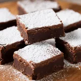 Quadrados de doce de chocolate com biscoito polvilhados com açúcar de confeiteiro sobre tábua de madeira