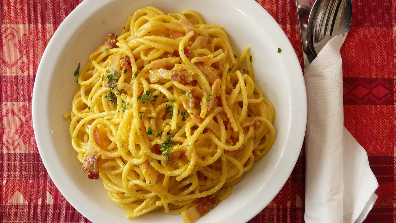 Prato de espaguete à carbonara com molho amarelo brilhante e sedoso envolvendo a massa, cubos de guanciale dourado e pimenta-do-reino