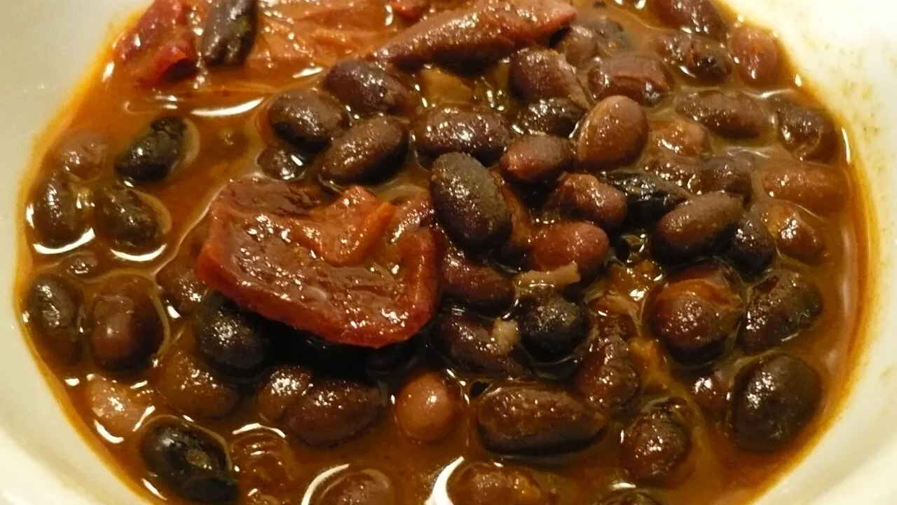 Panela de barro com feijoada vegetariana escura e encorpada, com legumes e couve refogada ao lado